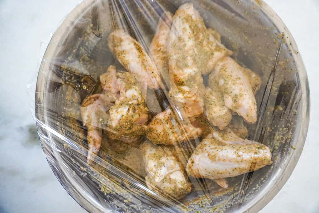 chicken wings marinating in a bowl covered with plastic wrap
