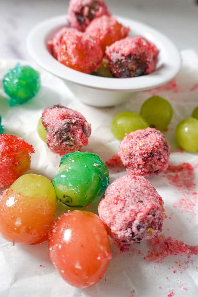 a close up view of a bowl of candy grapes with scattered grapes surrounding it