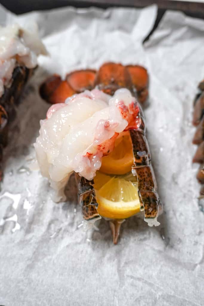 a hand peeling back a lobster tail with lemon wedges nestled in the shell