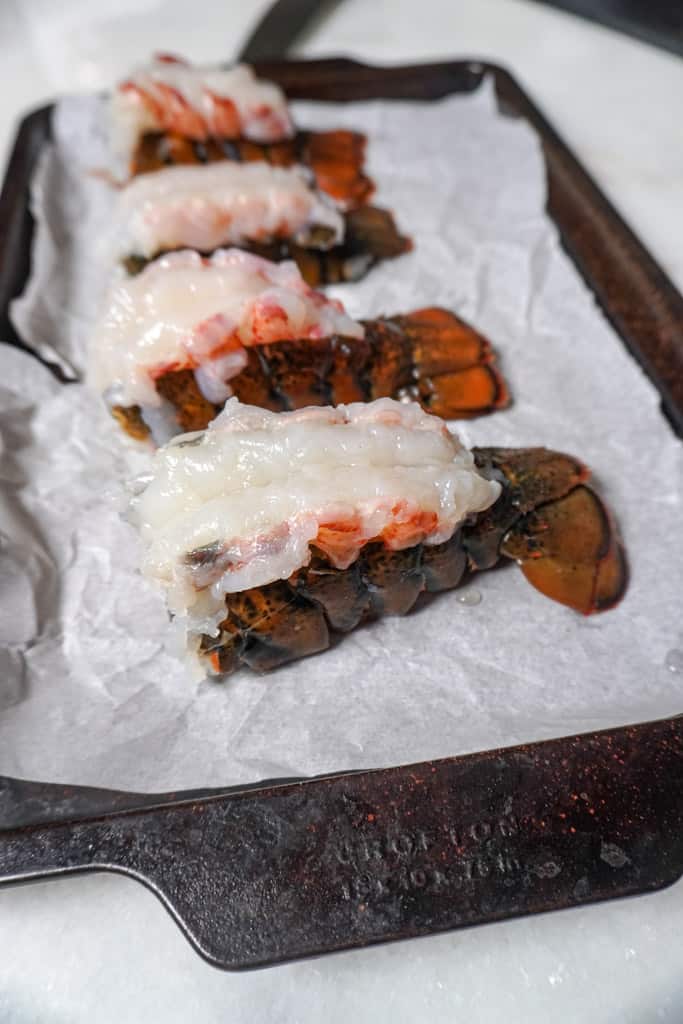four raw lobster tails on a baking sheet