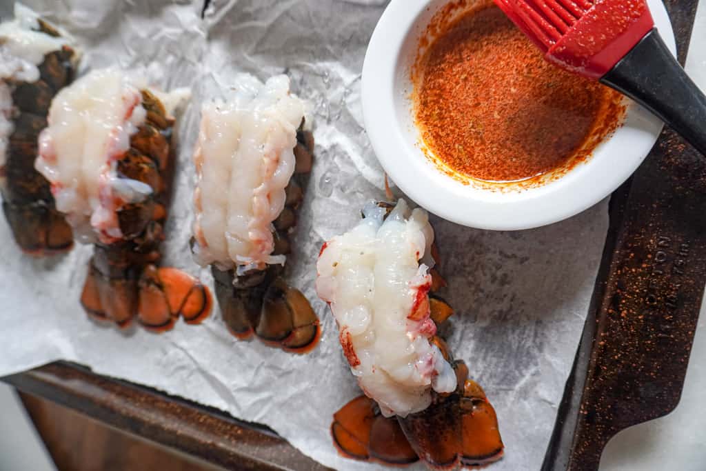 raw lobster tails on a baking sheet with a side of cajun butter seasoning