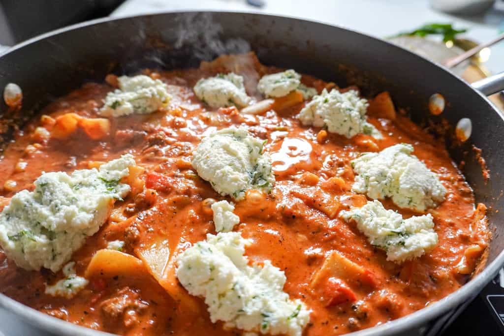close up view of a pot full of skillet lasagna topped with ricotta