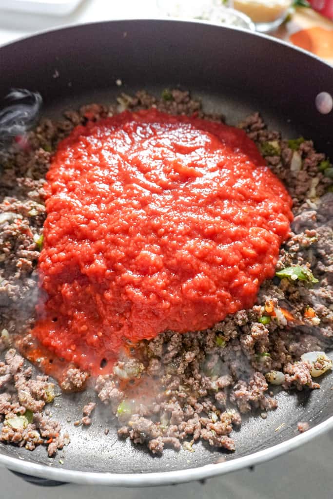 cooked ground beef in a pot, topped with tomato sauce