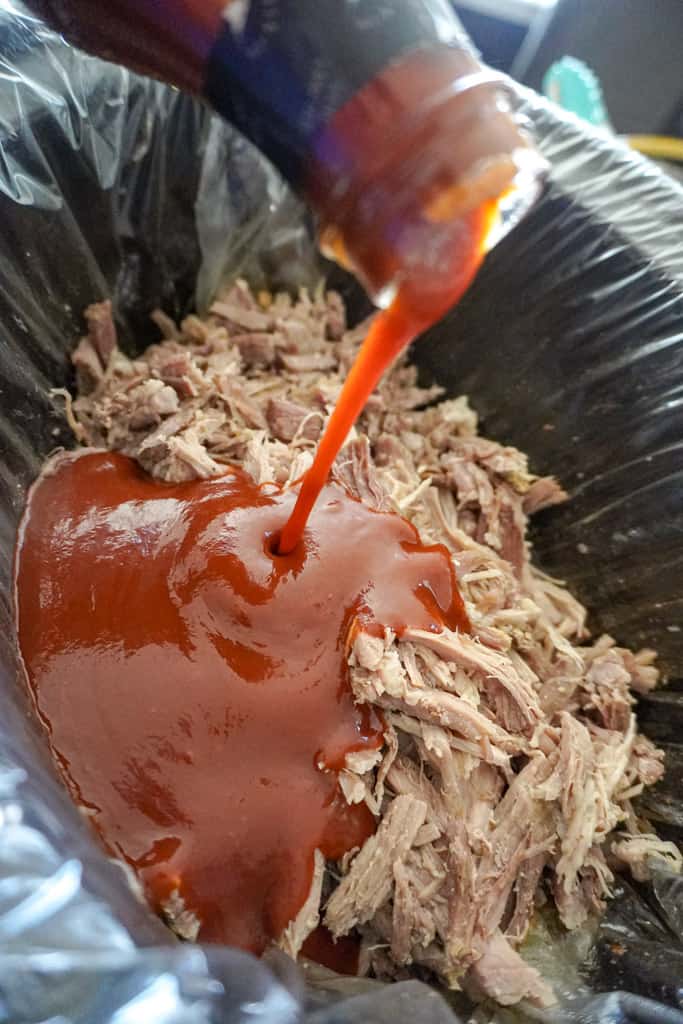 shredded pork in a slow cooker with bbq sauce being poured over it