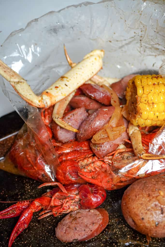 opened bag of seafood boil with crab legs, crawfish, andouille sausage, corn and potatoes