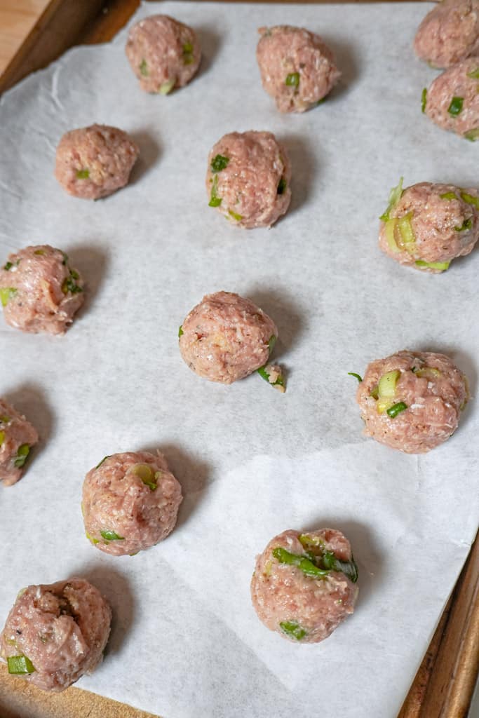 raw chicken meatballs on parchment paper lined baking sheet