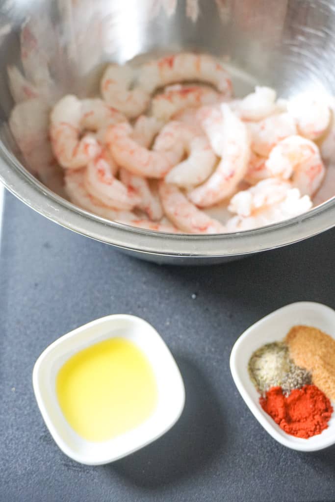 a bowl of raw shrimp, butter, and seasonings