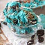 blue cookie monster ice cream in a clear bowl with small pieces of cookies around it
