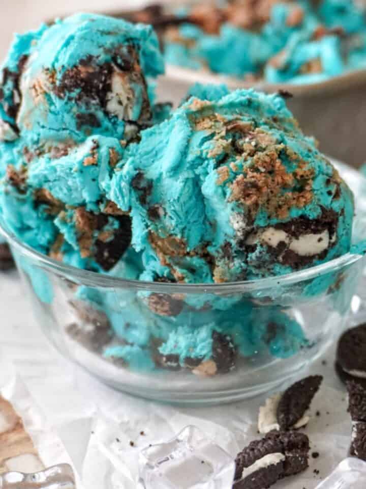 blue cookie monster ice cream in a clear bowl with small pieces of cookies around it
