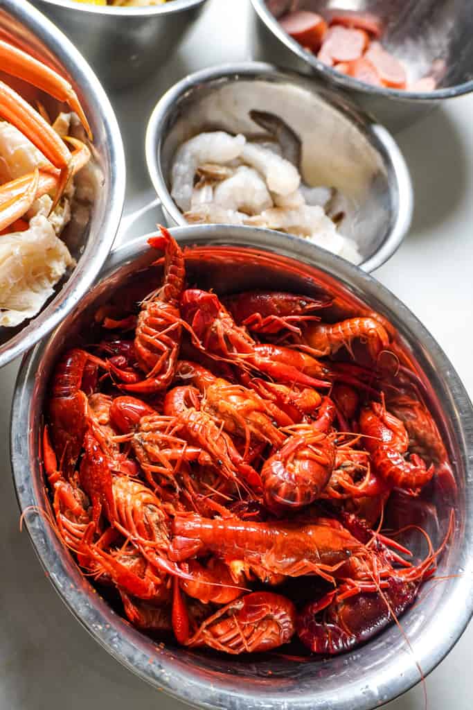 individual bowls of seafood boil bag ingredients, with crawfish at the forefront