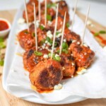 buffalo chicken meatballs on a platter with buffalo sauce in the background