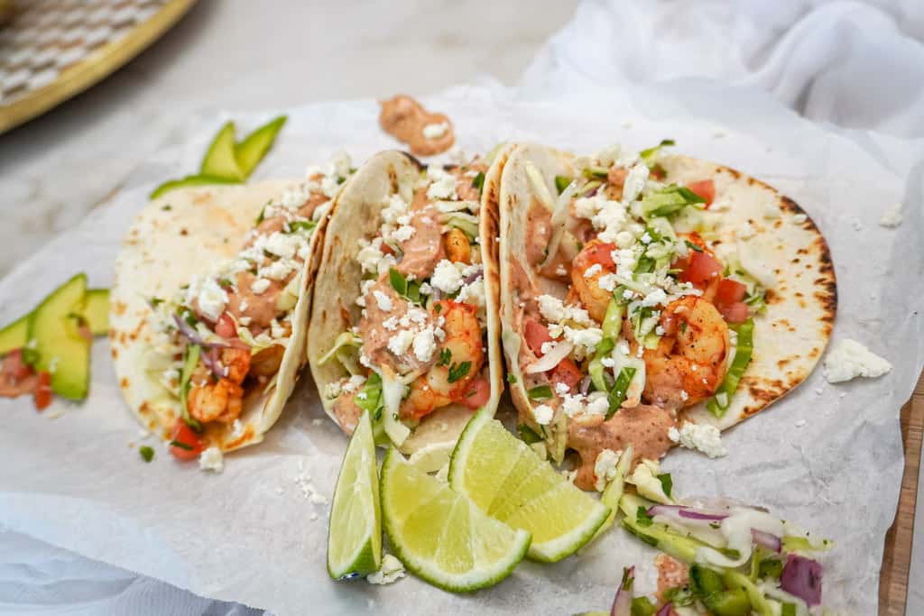 shrimp tacos sitting on a platter with cabbage slaw and other toppings and lime wedges on the side