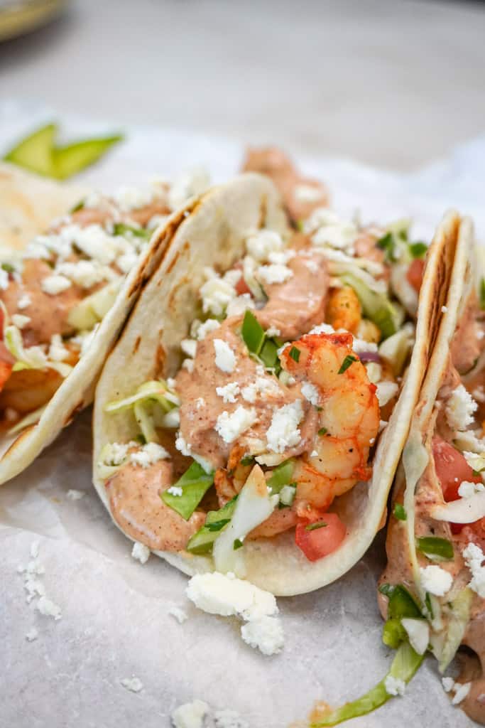 shrimp tacos with shredded lettuce, queso fresco, hot sauce, and lime wedges for serving