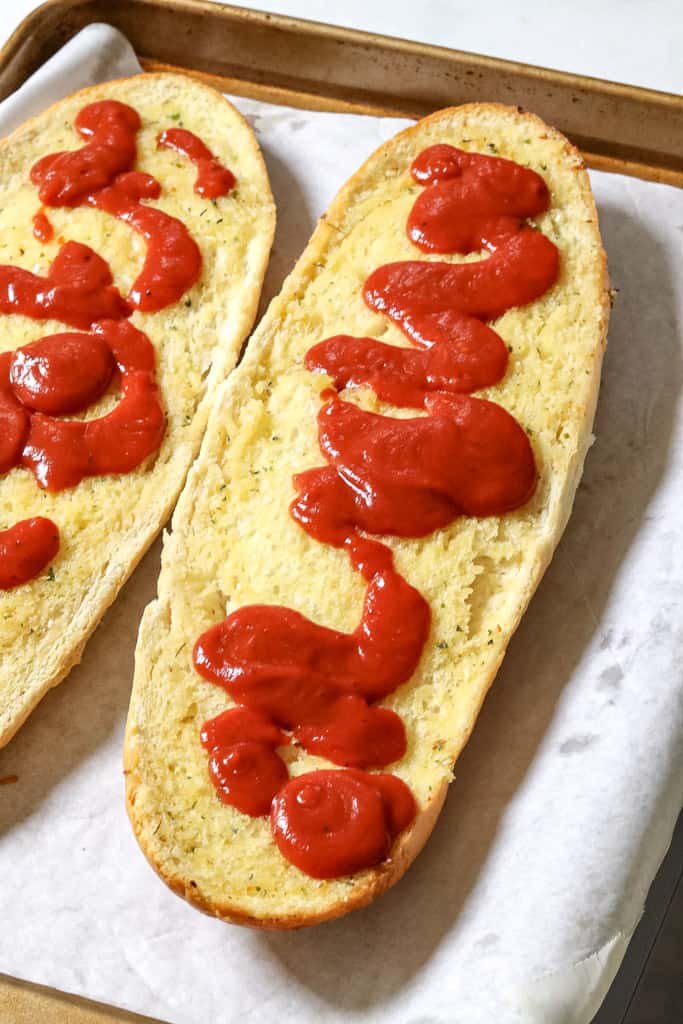 pizza sauce drizzled on two slices of french bread