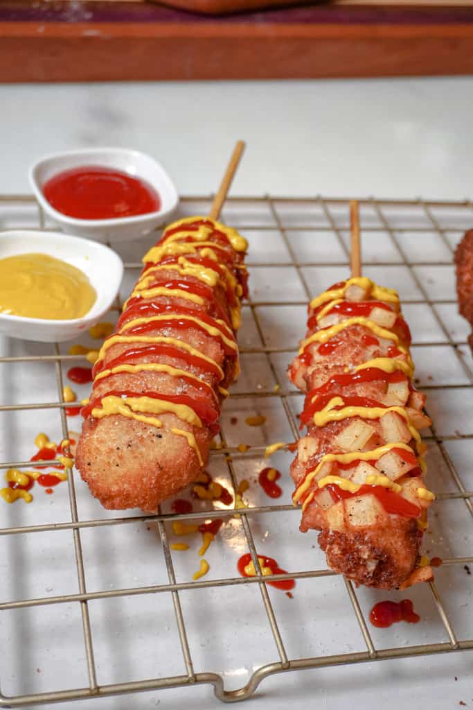 korean corn dogs on a cooling rack, drizzled with ketchup and mustard
