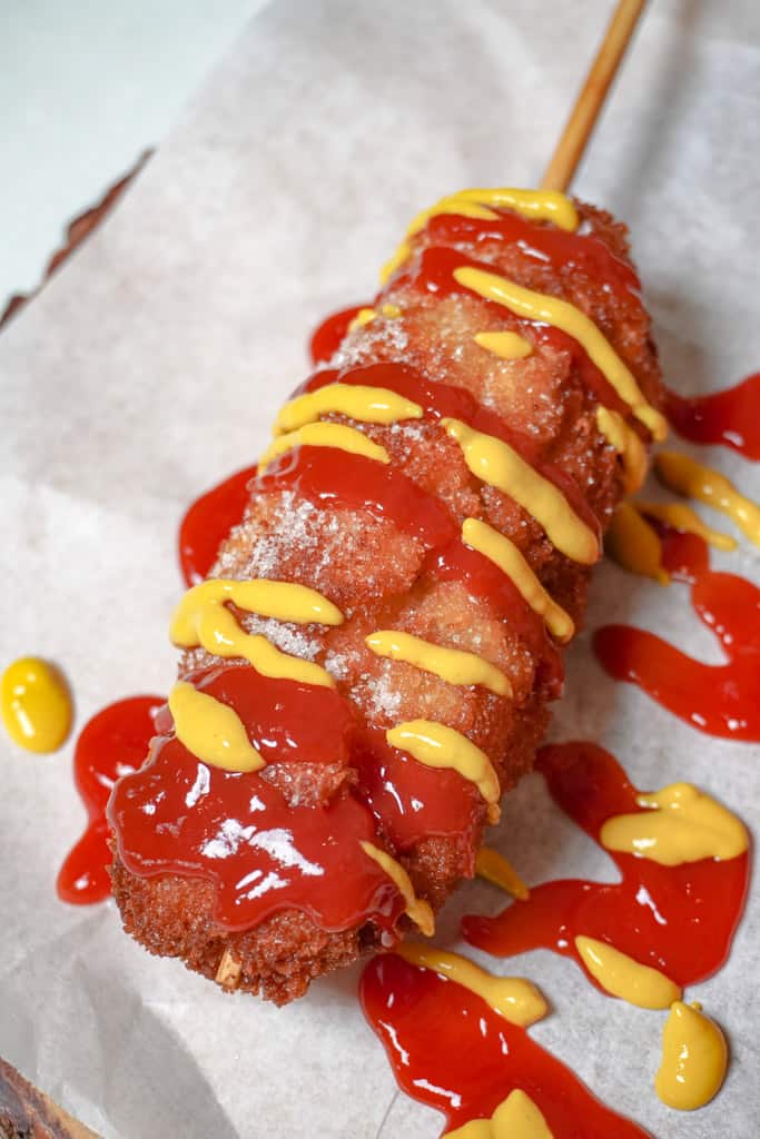 close up view of korean corn dog drizzled with mustard and ketchup