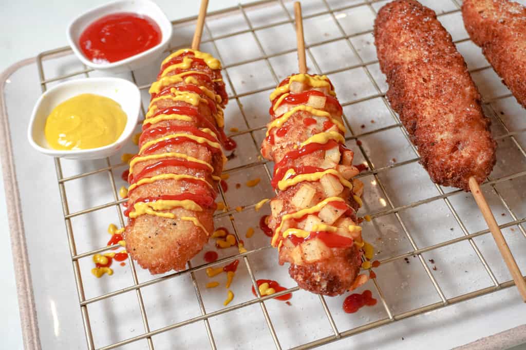 korean corn dogs on a cooling tray with mustard and ketchup in small saucers