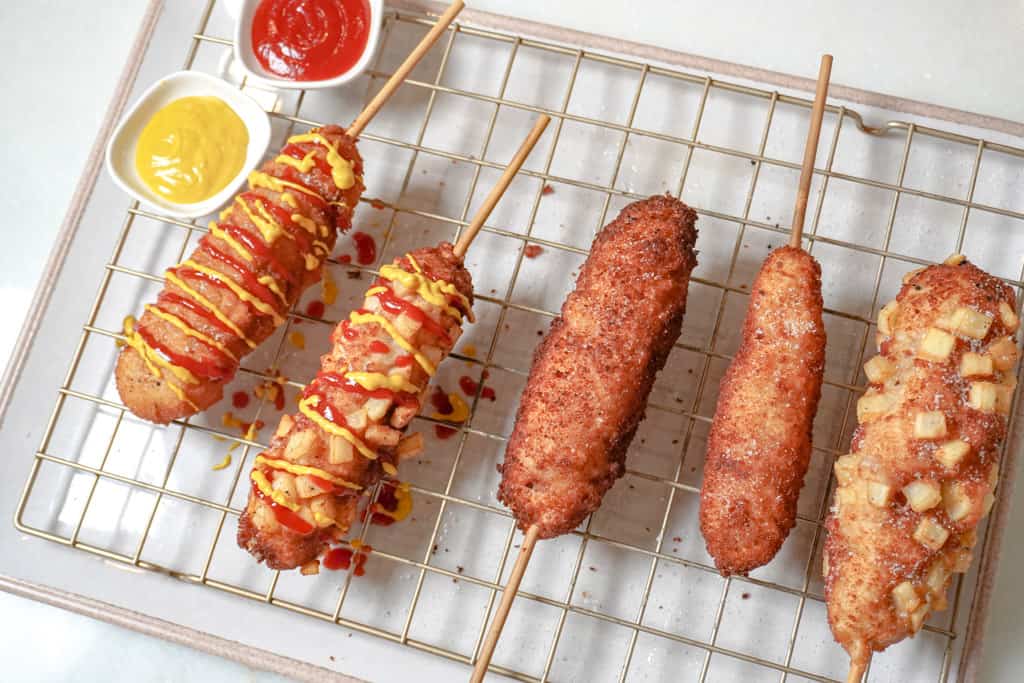 korean corn dogs on a cooling tray with mustard and ketchup in small saucers