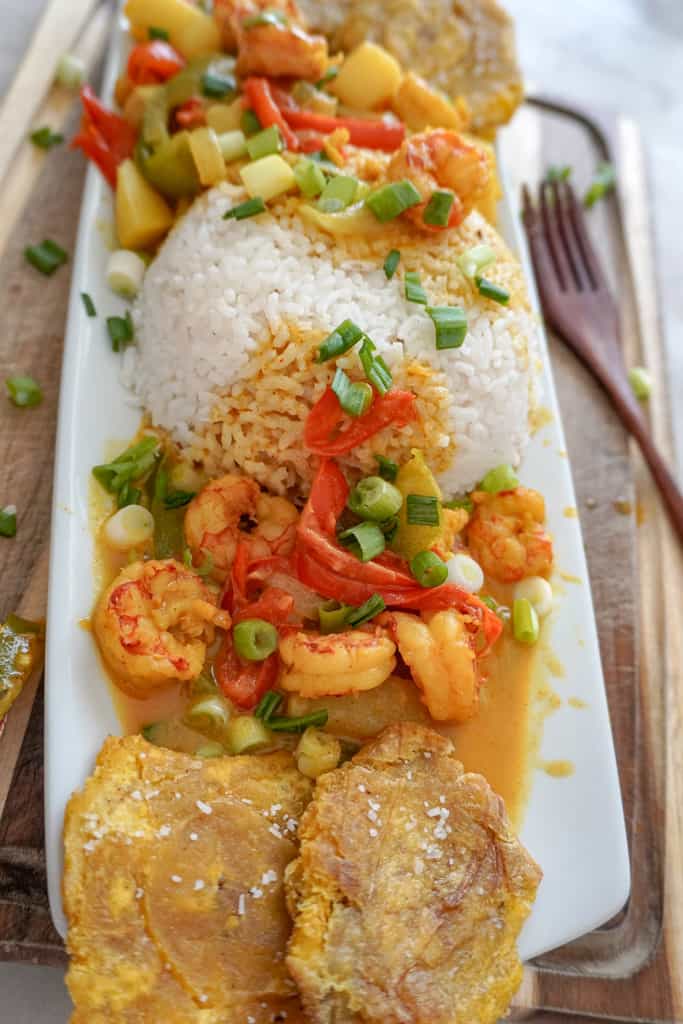 a plate of curry shrimp with rice and tostones