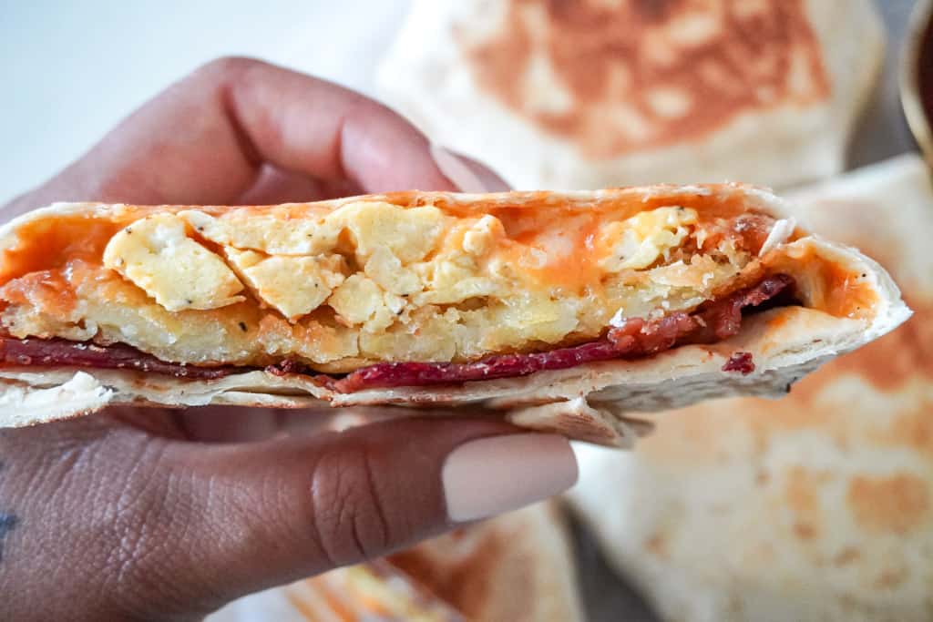 a hand holding a sliced breakfast crunch wrap to reveal the center