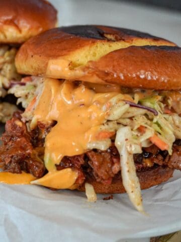 close up view of a brisket sandwich with coleslaw and sauce