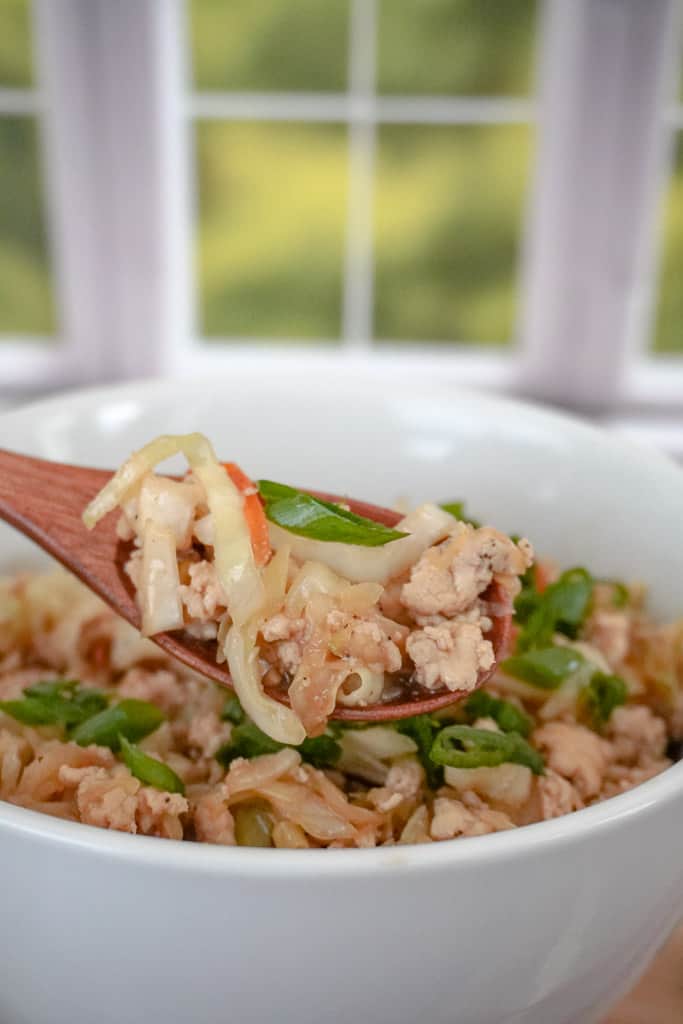 close up view of egg roll in a bowl with a spoonful hanging over the bowl