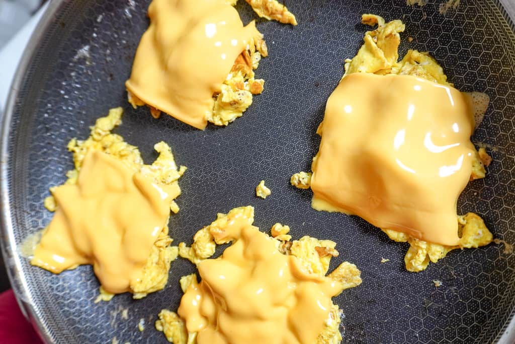 scrambled eggs in a skillet with melted cheddar cheese over each individual egg