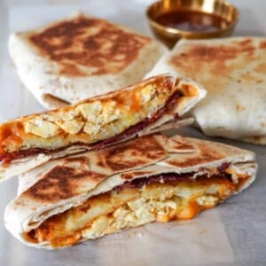 close up view of a sliced breakfast crunchwrap with more crunchwraps in the background with a small saucer of sauce