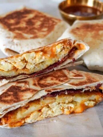 close up view of a sliced breakfast crunchwrap with more crunchwraps in the background with a small saucer of sauce