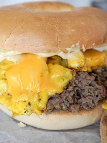 close up view of steak egg and cheese bagel with melty cheese on top of eggs and shaved steak
