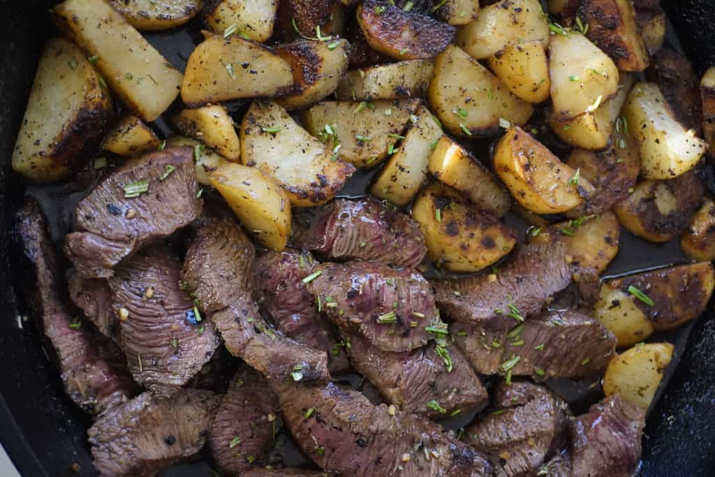 close up view of steak and potatoes in a skillet