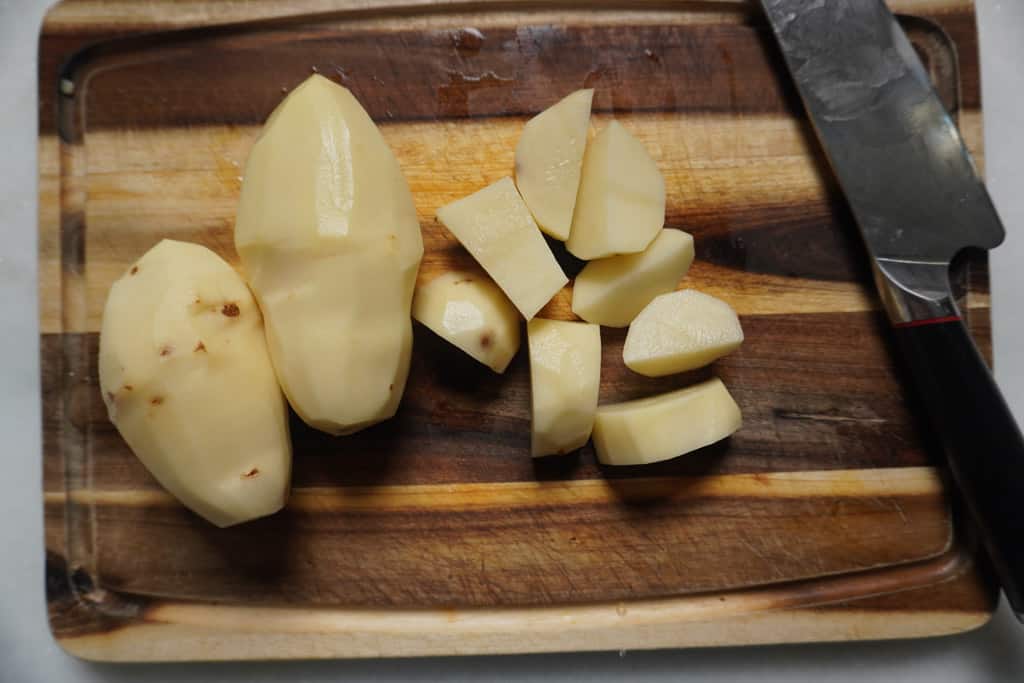 potatoes being skinned and sliced on a cutting board