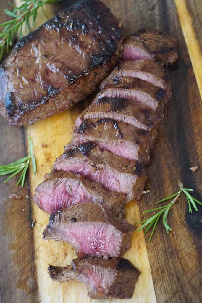 sliced flat iron steak beside a full filet with herbs