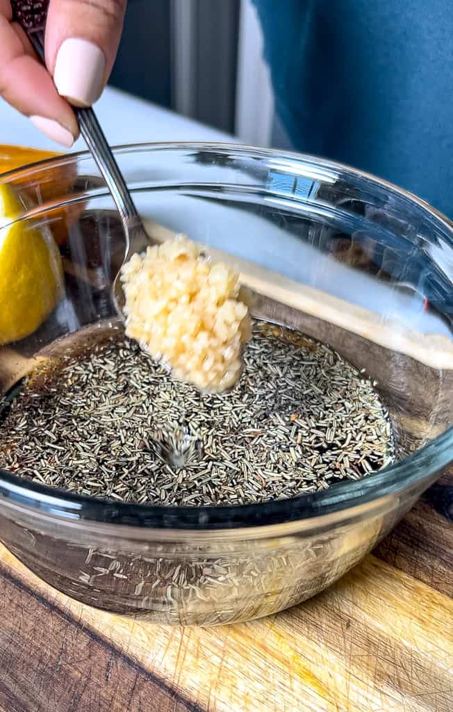 adding minced garlic to a bowl of ingredients for steak marinade