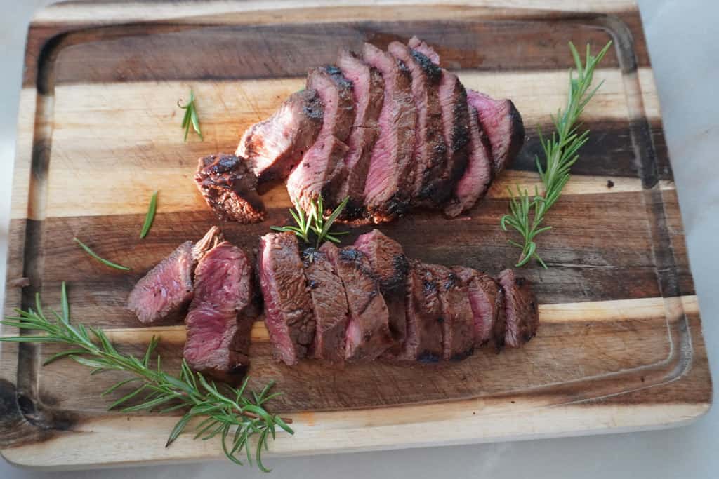 sliced flat iron steak on a cutting board with herbs