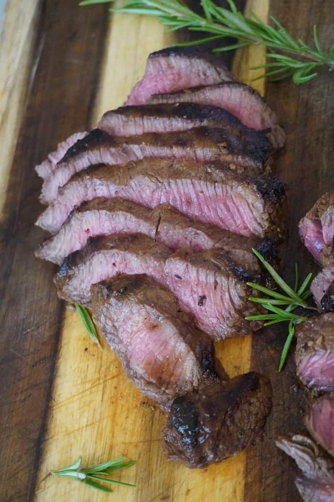 sliced steak surrounded by herbs on a cutting board