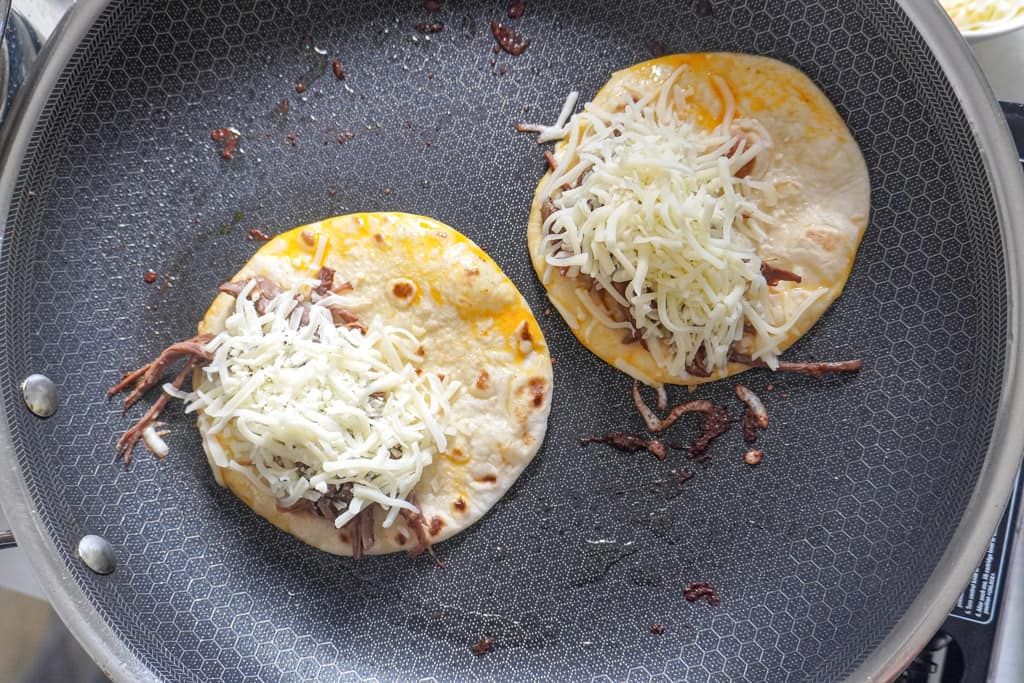 open faced tacos on a skillet with shredded brisket and cheese