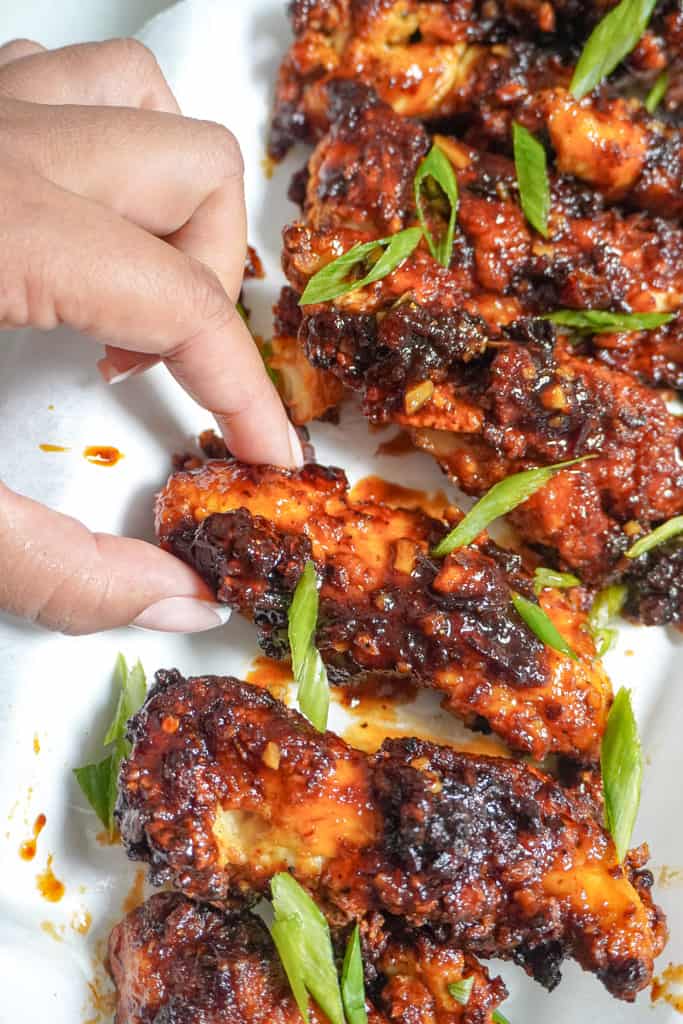 a hand reaching for a chipotle honey air fryer chicken tender on a plate