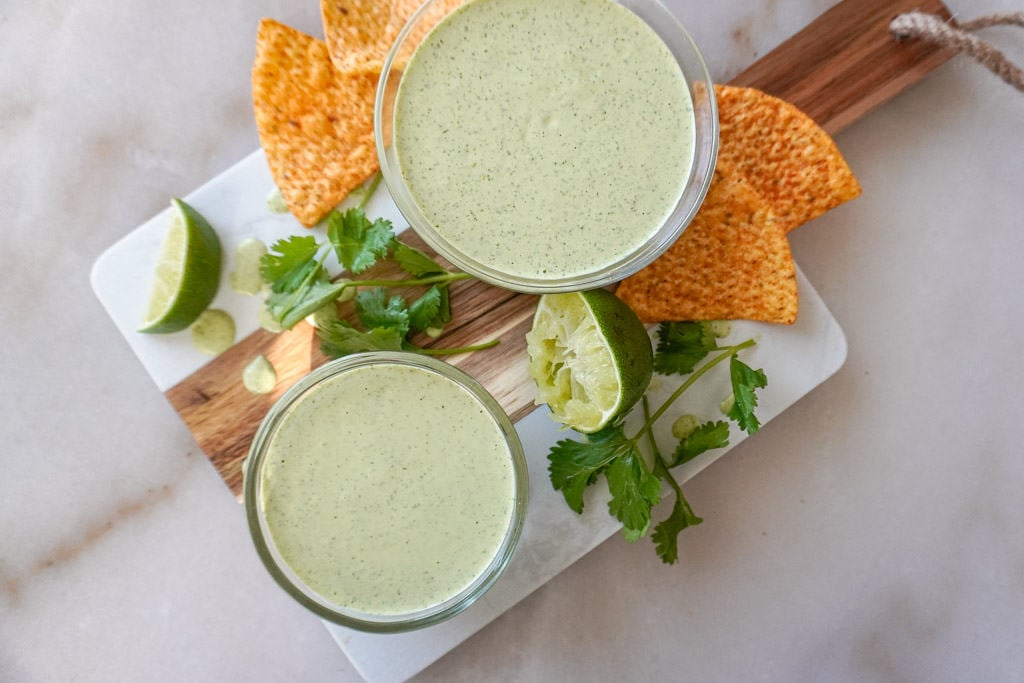 Homemade ranch dressing in two saucers on a cutting board with chips, lime, and cilantro