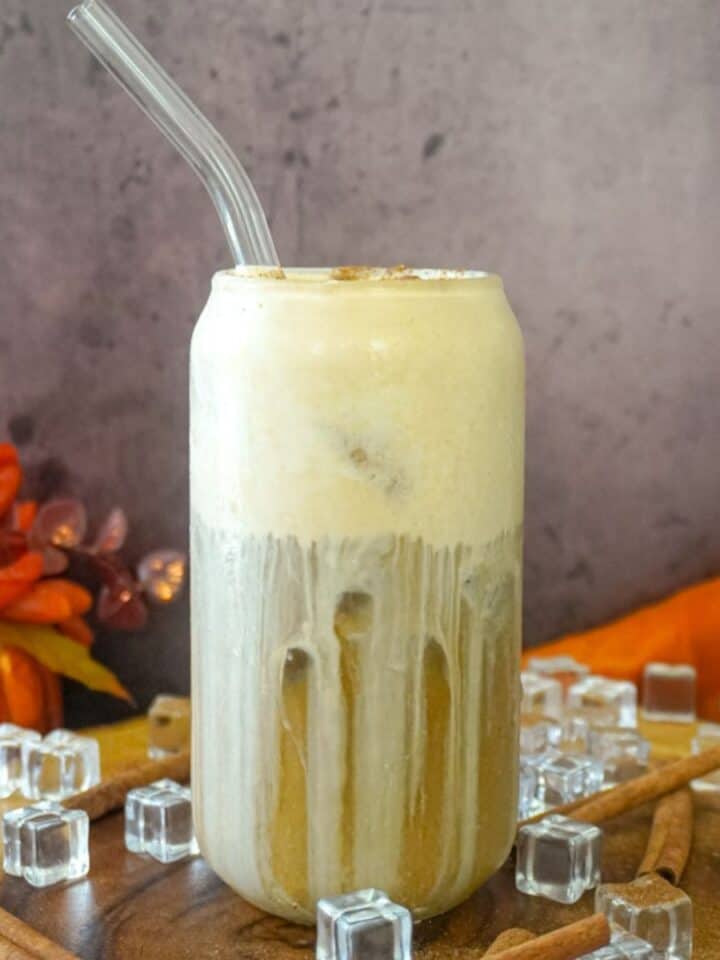a clear glass full of pumpkin cream cold brew with a straw inserted