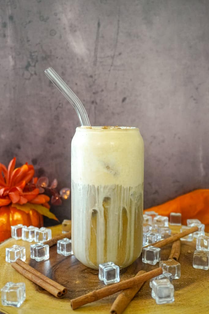 a clear glass full of pumpkin cream cold brew with a straw inserted
