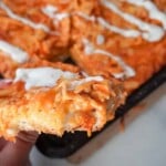 close up view of sheet pan buffalo chicken pizza with a hand holding one slice