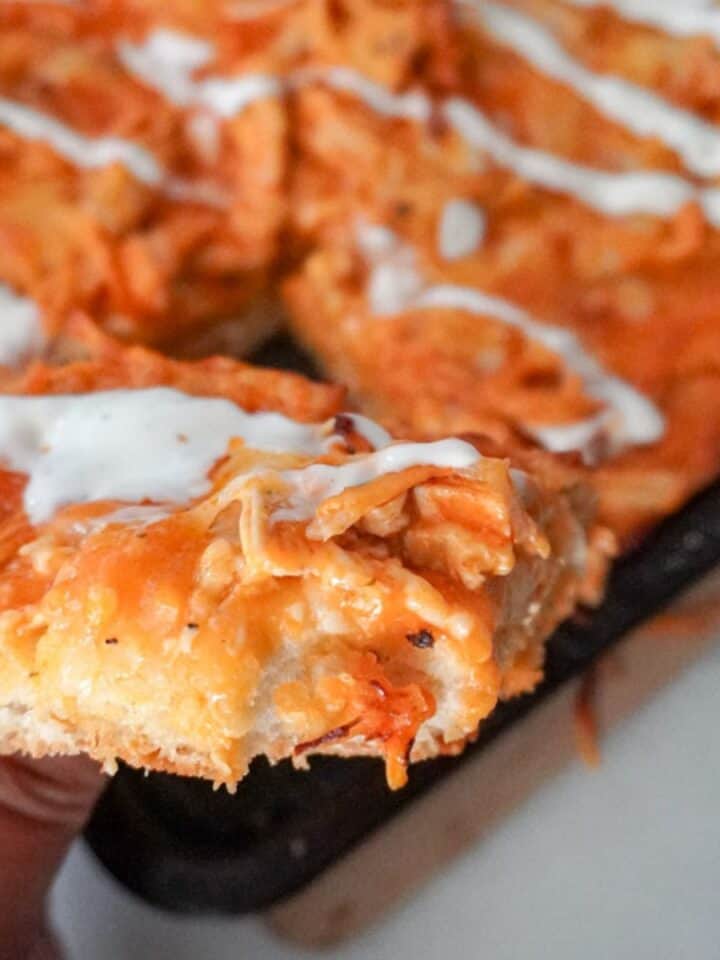 close up view of sheet pan buffalo chicken pizza with a hand holding one slice