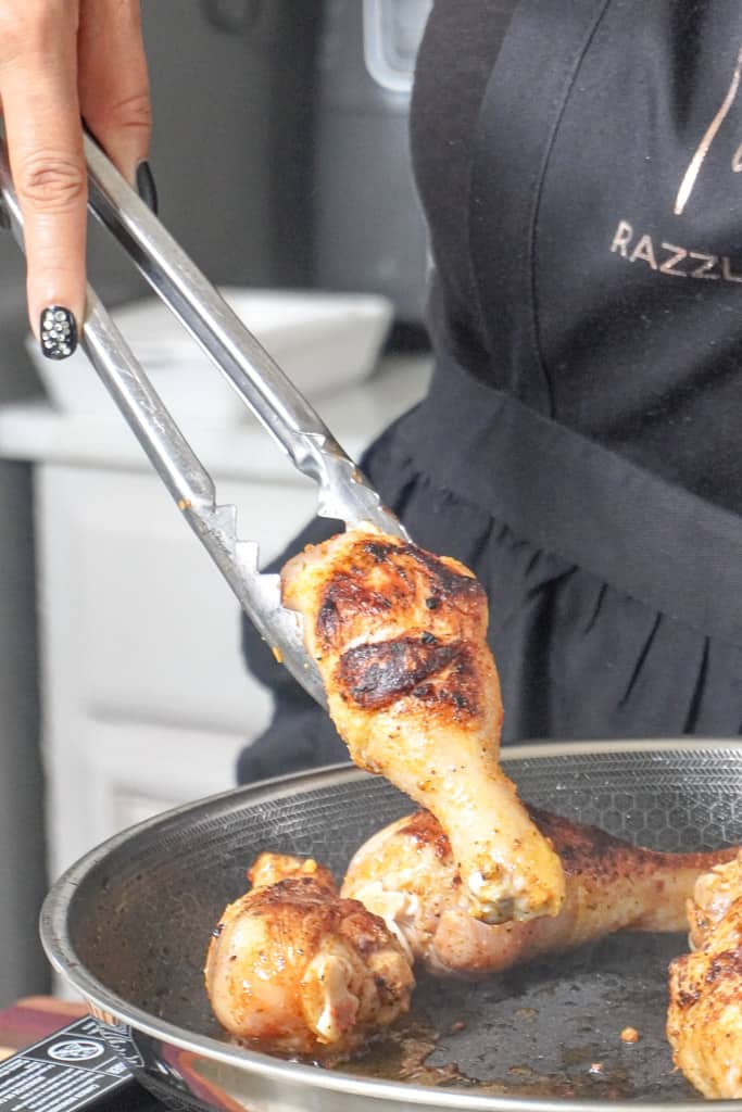 Tamara holding tongs and flipping chicken legs on a skillet