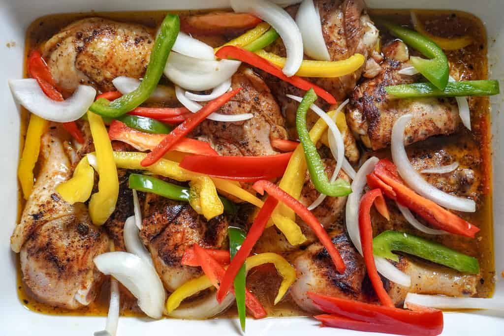 seared chicken added to a baking pan with sliced veggies