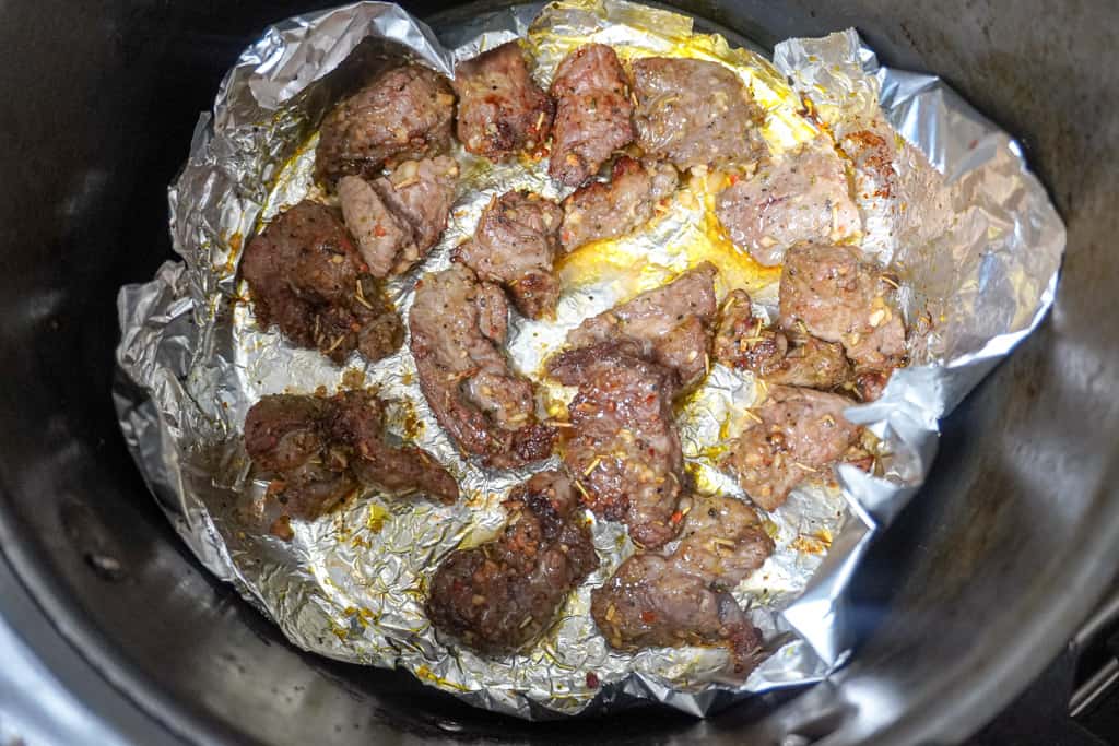steak bites in an air fryer basket lined with foil