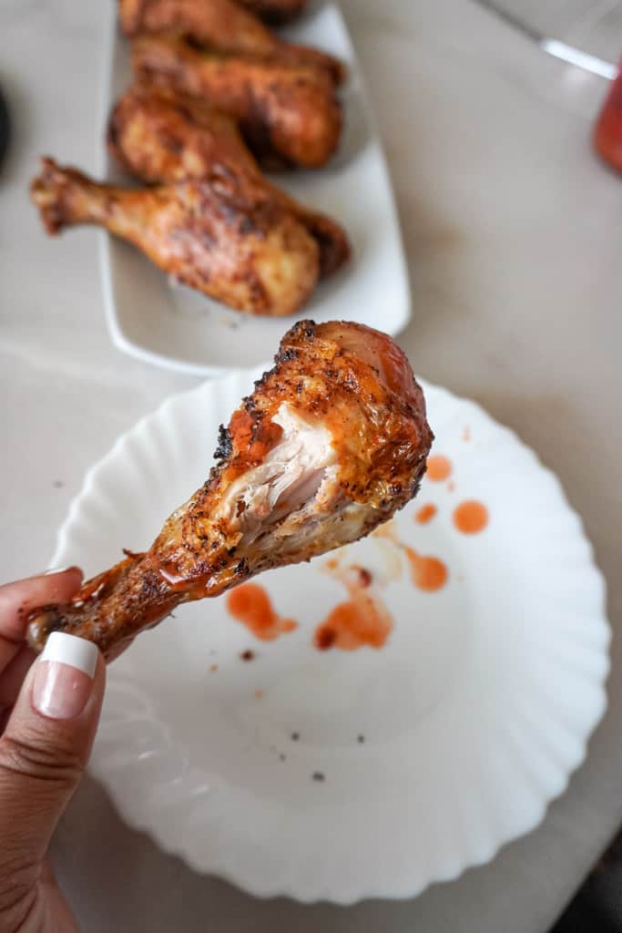a hand holding a bitten into chicken leg with a platter of more in the background