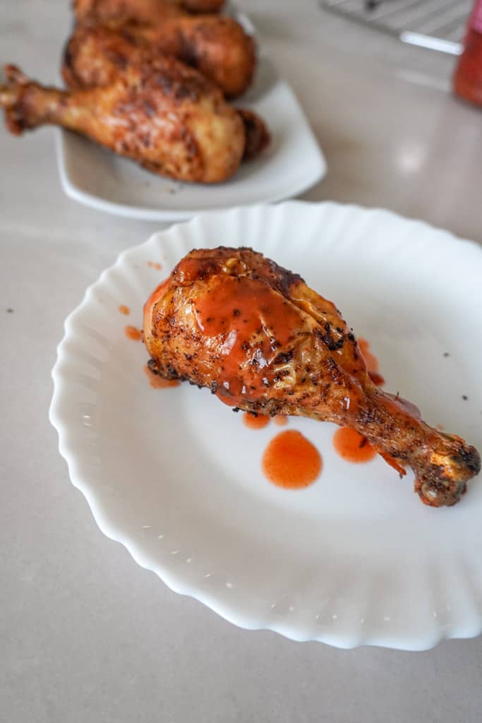 a chicken leg covered in hot sauce on a plate with a platter of more in the background