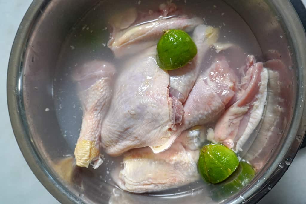 raw chicken in a bowl with water and limes