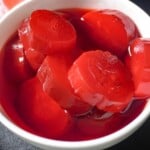strawberry kool aid pickles and blue raspberry pickles in a white bowl sitting on a cutting board